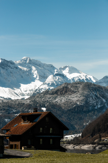 View of a charming Swiss chalet nestled against a backdrop of snow capped mountains under a serene blue sky captured from a moving train Train from Lucerne to Interlaken Switzerland. View of a charming Swiss chalet nestled against a backdrop of snow capped mountains under a serene blue sky captured from a moving train Train from Lucerne to Interlaken Switzerland.