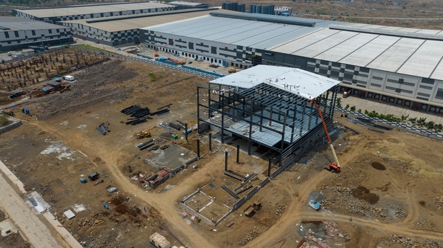 Aerial view of a warehouse construction site with steel framework heavy machinery and surrounding industrial buildings in Bhiwandi Maharashtra India. Aerial view of a warehouse construction site with steel framework heavy machinery and surrounding industrial buildings in Bhiwandi Maharashtra India.