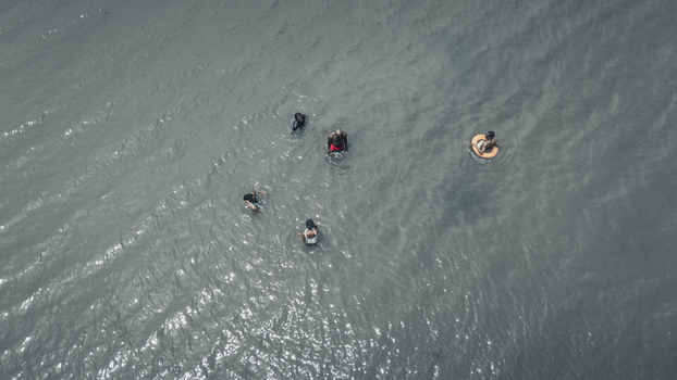 Aerial view of people swimming and floating in the grey rippled waters with one person in an orange lifebuoy Badagry Lagos Nigeria.