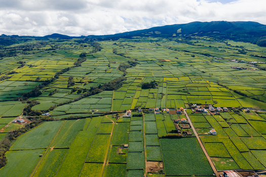 Aerial view of the lush green patchwork fields and stone walls of Terceira Island under a cloudy sky in Azores Portugal. Aerial view of the lush green patchwork fields and stone walls of Terceira Island under a cloudy sky in Azores Portugal.