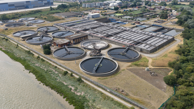 Aerial view of the Long Reach Sewage Treatment Works with circular sedimentation tanks and rectangular treatment basins located along the riverbank in Dartford England United Kingdom.