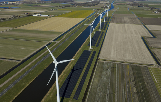 Aerial view of wind turbines and solar panels along a straight canal through flat agricultural fields in Netherlands. Aerial view of wind turbines and solar panels along a straight canal through flat agricultural fields in Netherlands.