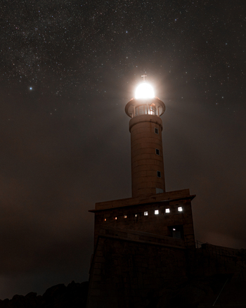 View of Faro de Punta Nariga lighthouse illuminated under a starry night sky with the Milky Way visible in Malpica A Coruna Spain. View of Faro de Punta Nariga lighthouse illuminated under a starry night sky with the Milky Way visible in Malpica A Coruna Spain.