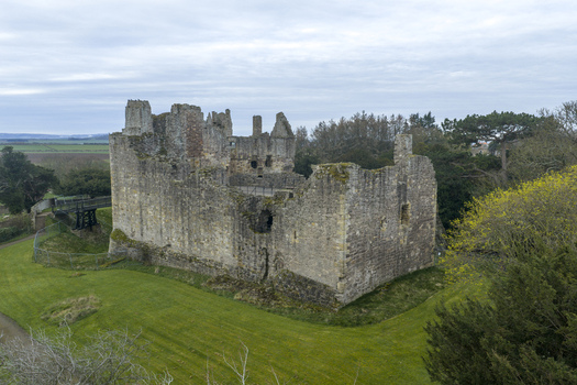 Aerial view of Dirleton Castle and Gardens featuring the historic ruined stone walls and lush green lawns under an overcast sky in Dirleton Scotland United Kingdom. Aerial view of Dirleton Castle and Gardens featuring the historic ruined stone walls and lush green lawns under an overcast sky in Dirleton Scotland United Kingdom.