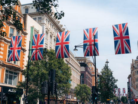 London United Kingdom 20 June 2025 View of Union Jack flags fluttering above a bustling London street casting shadows on the vibrant facades and lush green trees below. London United Kingdom 20 June 2025 View of Union Jack flags fluttering above a bustling London street casting shadows on the vibrant facades and lush green trees below.