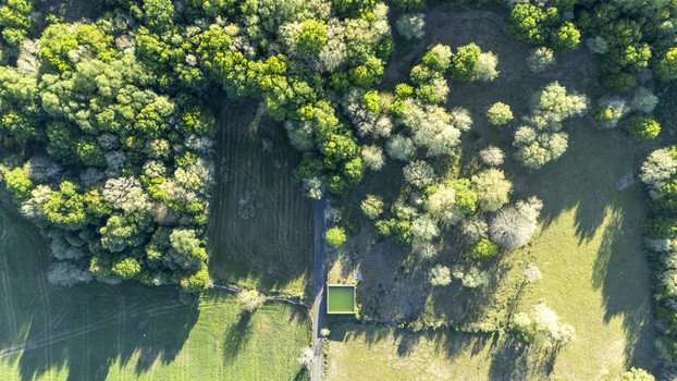 Aerial view of lush green forest canopy open meadows and a small square water tank beside a narrow rural road Ourense Province of Ourense Spain. Aerial view of lush green forest canopy open meadows and a small square water tank beside a narrow rural road Ourense Province of Ourense Spain.