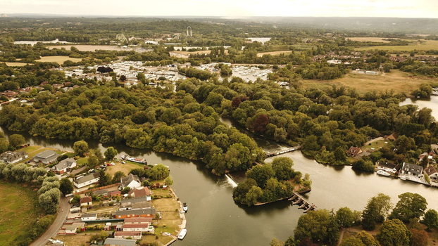 Aerial view of the River Thames with lush trees a weir small boats and residential houses along the riverbank in Thames United Kingdom. Aerial view of the River Thames with lush trees a weir small boats and residential houses along the riverbank in Thames United Kingdom.