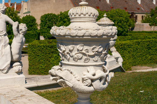 View of an ornate stone garden vase featuring intricate carvings of sea creatures and foliage at the Belvedere Palace gardens with cherub statues and manicured hedges Vienna Vienna Austria. View of an ornate stone garden vase featuring intricate carvings of sea creatures and foliage at the Belvedere Palace gardens with cherub statues and manicured hedges Vienna Vienna Austria.