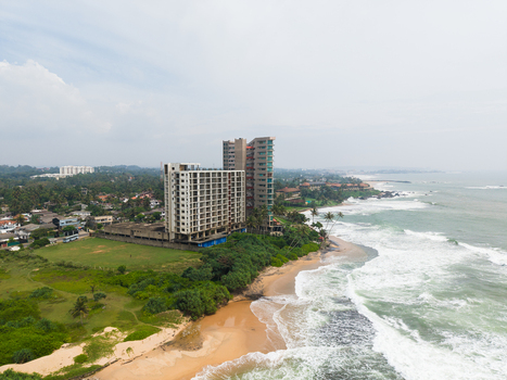 Aerial view of modern high rise buildings along the sandy coastline with crashing waves and lush tropical greenery under a cloudy sky in Galle Southern Province Sri Lanka. Aerial view of modern high rise buildings along the sandy coastline with crashing waves and lush tropical greenery under a cloudy sky in Galle Southern Province Sri Lanka.