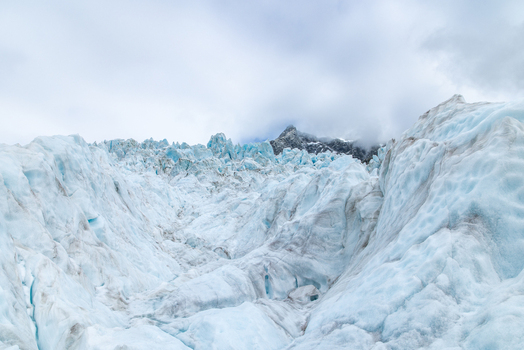 View of the vast glacier with rugged ice formations under a cloudy sky a majestic contrast of white blue and gray in Franz Josef Glacier West Coast Region New Zealand. View of the vast glacier with rugged ice formations under a cloudy sky a majestic contrast of white blue and gray in Franz Josef Glacier West Coast Region New Zealand.