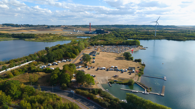 Aerial view of Stewartby Lake featuring a parking area with cars and caravans surrounded by trees and water with a wind turbine and industrial structures in Bedford England United Kingdom. Aerial view of Stewartby Lake featuring a parking area with cars and caravans surrounded by trees and water with a wind turbine and industrial structures in Bedford England United Kingdom.