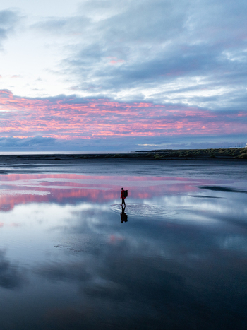 Aerial view of a solitary figure standing on the reflective shores of Stokksnes gazing into the vibrant pink tinged horizon Höfn Iceland. Aerial view of a solitary figure standing on the reflective shores of Stokksnes gazing into the vibrant pink tinged horizon Höfn Iceland.