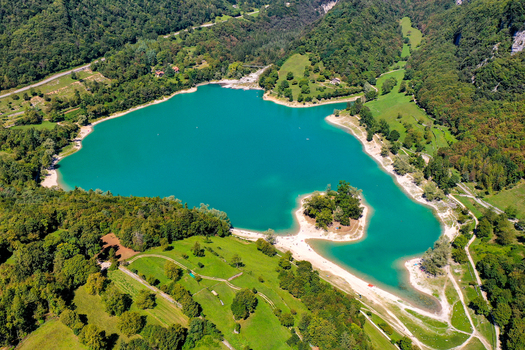 Aerial view of the turquoise waters of Lago di Tenno featuring a small wooded island and surrounding lush green forests in Tenno Trentino Alto Adige Italy.