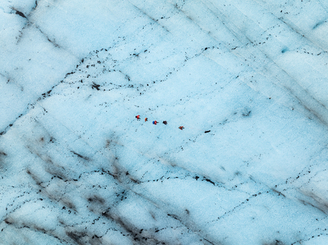 Aerial view of Breidamerkurjokull glacier with a small group of hikers in colorful gear trekking across the vast blue ice surface in Sveitarfelagid Hornafjordur Iceland. Aerial view of Breidamerkurjokull glacier with a small group of hikers in colorful gear trekking across the vast blue ice surface in Sveitarfelagid Hornafjordur Iceland.