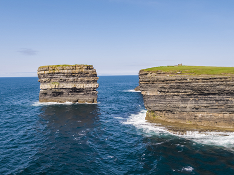 Aerial view of the Dun Briste sea stack with its distinct layered rock formations rising from the deep blue Atlantic ocean off the coast of County Mayo Ireland. Aerial view of the Dun Briste sea stack with its distinct layered rock formations rising from the deep blue Atlantic ocean off the coast of County Mayo Ireland.