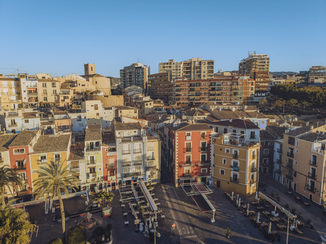 Aerial view of colorful traditional houses a town square with outdoor seating and palm trees under a clear blue sky in La Vila Joiosa Valencian Community Spain. Aerial view of colorful traditional houses a town square with outdoor seating and palm trees under a clear blue sky in La Vila Joiosa Valencian Community Spain.