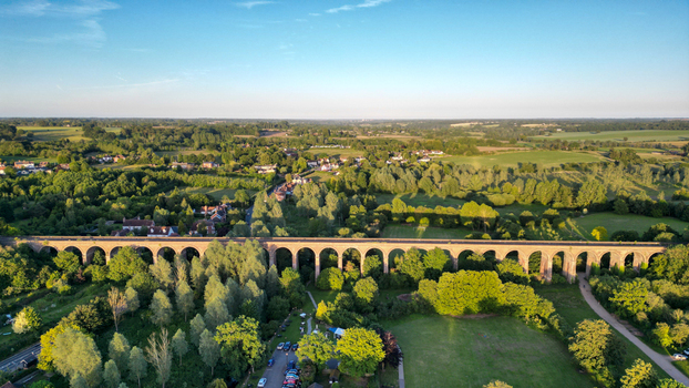 Aerial view of the historic Chappel Viaduct spanning the lush green countryside with surrounding trees and rural landscape in Chappel England United Kingdom.
