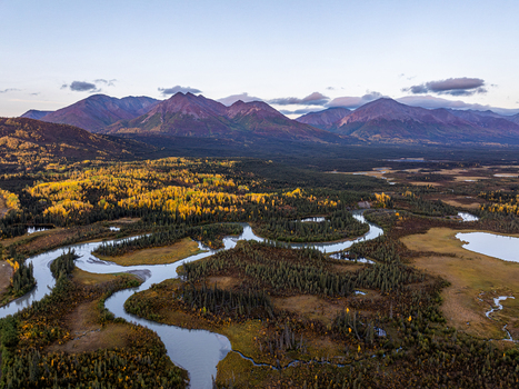 Aerial view of a winding river flowing through a valley with vibrant autumn foliage and distant mountains in Slana Alaska United States. Aerial view of a winding river flowing through a valley with vibrant autumn foliage and distant mountains in Slana Alaska United States.
