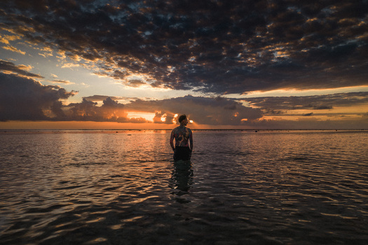 Aerial view of a man with tattoos standing in the shallow ocean water during a dramatic sunset with dark clouds over the horizon in Moka District Mauritius. Aerial view of a man with tattoos standing in the shallow ocean water during a dramatic sunset with dark clouds over the horizon in Moka District Mauritius.