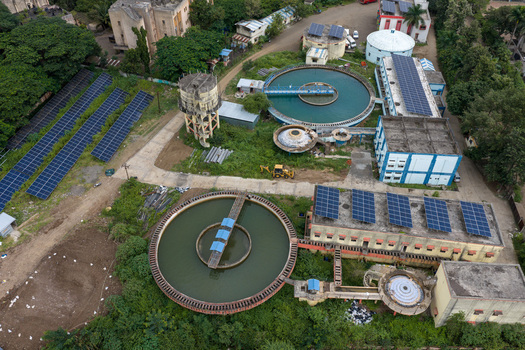Aerial view of a water treatment plant featuring large circular sedimentation tanks solar panel arrays on rooftops and the ground and industrial infrastructure in Karad Maharashtra India.
