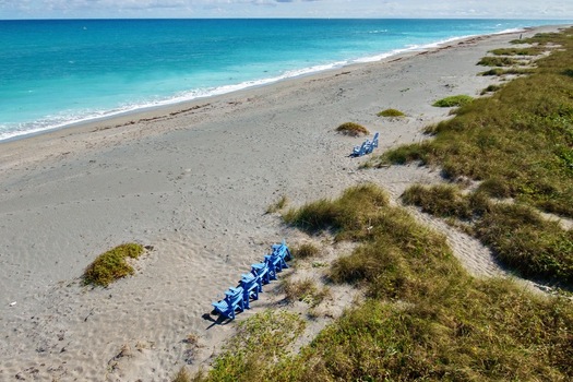Aerial view of turquoise waters meet the sandy shore of Jupiter Island with blue chairs dotting the landscape Jupiter Island Florida United States.