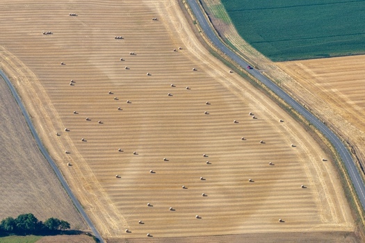 Aerial view of a harvested wheat field dotted with numerous hay bales bordered by a rural road and surrounding agricultural landscape in Hombourg Grand Est France. Aerial view of a harvested wheat field dotted with numerous hay bales bordered by a rural road and surrounding agricultural landscape in Hombourg Grand Est France.