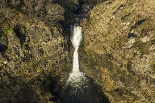 Aerial view of Lealt Falls cascading down a steep rocky cliff into a dark pool surrounded by rugged terrain Isle of Skye Scotland United Kingdom. Aerial view of Lealt Falls cascading down a steep rocky cliff into a dark pool surrounded by rugged terrain Isle of Skye Scotland United Kingdom.