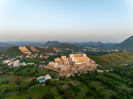 Aerial view of a large resort complex nestled among the Aravalli hills with lush green fields and surrounding landscape in Udaipur Rajasthan India.