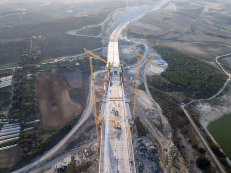 Aerial view of a massive bridge under construction featuring tall yellow cranes and concrete segments extending over a rural landscape in Istanbul Istanbul Turkiye.