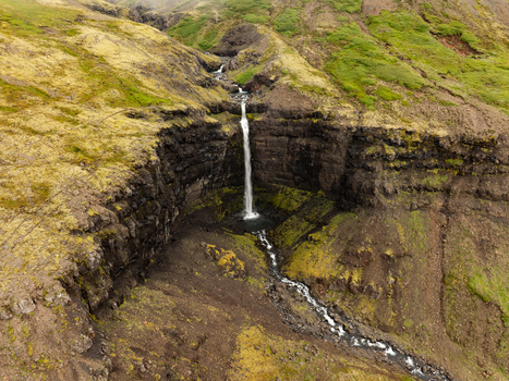 Aerial view of Flogufoss waterfall cascading over dark basalt cliffs surrounded by mossy green terrain in Disarstadir Fjardabyggd Iceland.