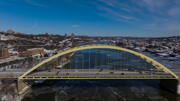 Aerial view of the yellow Daniel Carter Beard Bridge spanning the icy Ohio River with snowy banks and city buildings under a clear blue sky Cincinnati Ohio United States. Aerial view of the yellow Daniel Carter Beard Bridge spanning the icy Ohio River with snowy banks and city buildings under a clear blue sky Cincinnati Ohio United States.