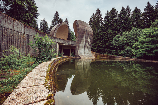 View of the Korcanica Memorial Zone with concrete monuments reflected in a pool of water surrounded by a pine forest in Sanski Most Federation of Bosnia Bosnia and Herzegovina. View of the Korcanica Memorial Zone with concrete monuments reflected in a pool of water surrounded by a pine forest in Sanski Most Federation of Bosnia Bosnia and Herzegovina.