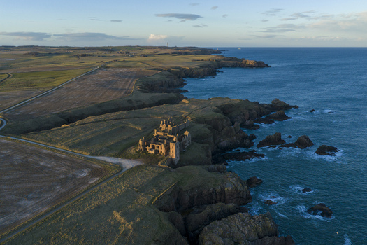 Aerial view of the ruined Slains Castle perched on rugged cliffs overlooking the North Sea and surrounding green fields Cruden Bay Scotland United Kingdom. Aerial view of the ruined Slains Castle perched on rugged cliffs overlooking the North Sea and surrounding green fields Cruden Bay Scotland United Kingdom.