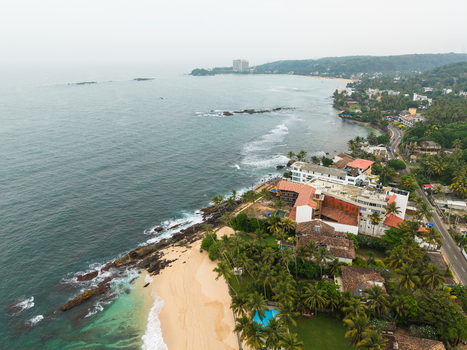 Aerial view of the tropical coastline with sandy beaches palm trees and coastal resorts along the turquoise ocean under an overcast sky in Unawatuna Southern Province Sri Lanka.