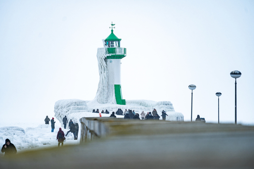 View of the ice covered Molenfeuer Sassnitz lighthouse on a pier with people walking in the cold winter weather in Sassnitz Mecklenburg Vorpommern Germany.