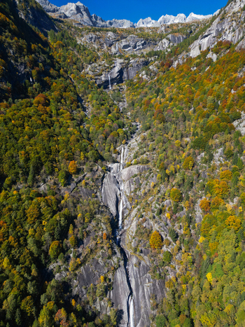 Aerial view of the Val di Mello waterfall cascading down steep granite cliffs surrounded by vibrant autumn foliage and jagged mountain peaks in Val Masino Lombardia Italy. Aerial view of the Val di Mello waterfall cascading down steep granite cliffs surrounded by vibrant autumn foliage and jagged mountain peaks in Val Masino Lombardia Italy.