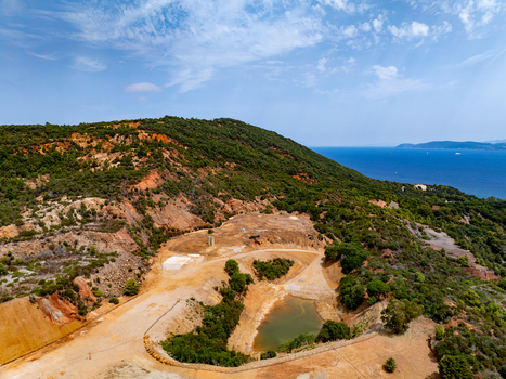 Aerial view of the historic iron mine area near Laghetto delle conche featuring rugged red geology sparse vegetation and a pond overlooking the sea in Rio Marina Toscana Italy.
