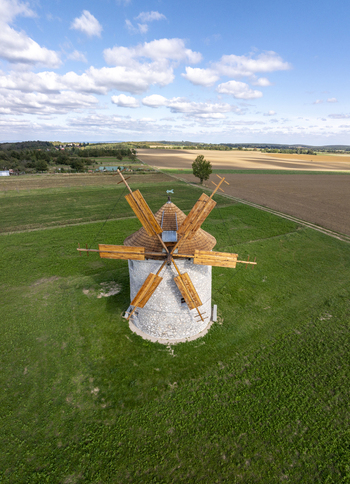 Aerial view of the historic Regi Szelmalom windmill featuring its stone structure and wooden blades set amidst green fields and agricultural land in Tes Hungary. Aerial view of the historic Regi Szelmalom windmill featuring its stone structure and wooden blades set amidst green fields and agricultural land in Tes Hungary.
