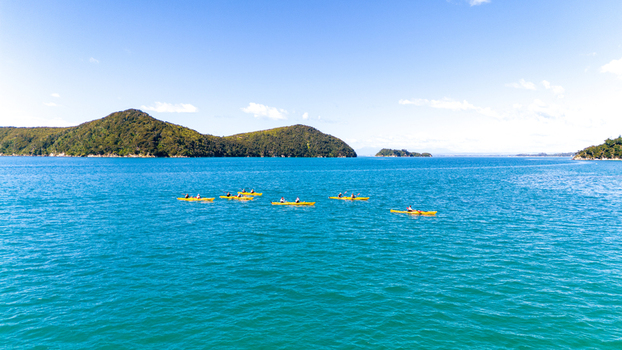 Aerial view of kayaks glide across the turquoise waters towards the lush green islands of Abel Tasman National Park Abel Tasman National Park Tasman Region New Zealand. Aerial view of kayaks glide across the turquoise waters towards the lush green islands of Abel Tasman National Park Abel Tasman National Park Tasman Region New Zealand.