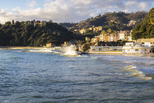 View of Venere Azzurra beach with waves crashing against the shore and colorful buildings on the hillside in Lerici Liguria Italy.