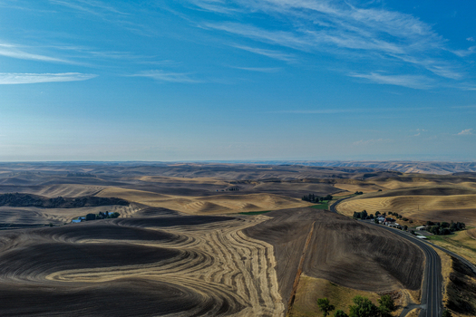Aerial view of the rolling hills of the Palouse region featuring harvested fields dark soil and a winding road under a clear blue sky in Palouse Washington United States. Aerial view of the rolling hills of the Palouse region featuring harvested fields dark soil and a winding road under a clear blue sky in Palouse Washington United States.