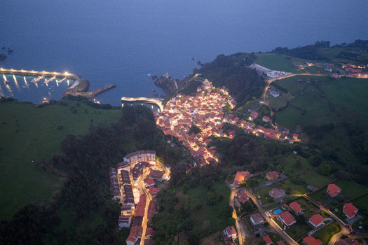 Aerial view of the illuminated coastal town of Cudillero at dusk with glowing streetlights a harbor and lush green hills overlooking the sea in Cudillero Asturias Spain. Aerial view of the illuminated coastal town of Cudillero at dusk with glowing streetlights a harbor and lush green hills overlooking the sea in Cudillero Asturias Spain.