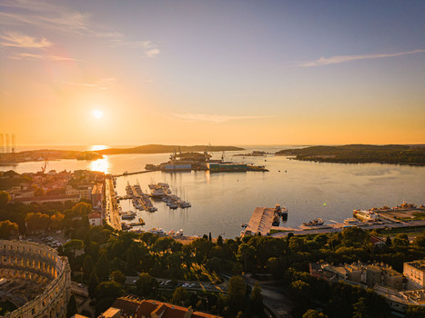 Aerial view of the sun setting over the Adriatic Sea casting a golden glow on the ancient Roman amphitheater and the bustling harbor Pula Istria County Croatia.