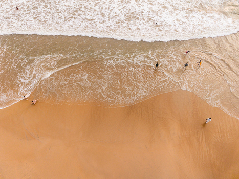 Aerial view of people relaxing and walking on a golden sandy beach with gentle ocean waves washing ashore in Galle Southern Province Sri Lanka.