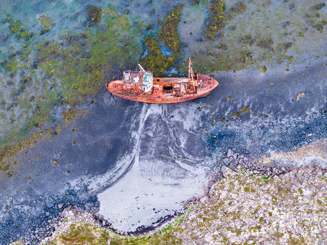 Aerial view of a rusted shipwreck stranded on a dark volcanic sand beach with mossy rocks and shallow coastal waters in Iceland. Aerial view of a rusted shipwreck stranded on a dark volcanic sand beach with mossy rocks and shallow coastal waters in Iceland.