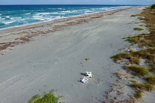Aerial view of white chairs sitting on the sandy beach where the turquoise waves meet the shore Jupiter Island Florida United States. Aerial view of white chairs sitting on the sandy beach where the turquoise waves meet the shore Jupiter Island Florida United States.