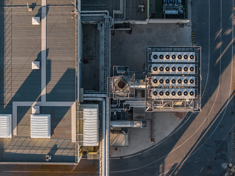 Aerial view of an industrial plant featuring rooftop HVAC units complex piping systems and long shadows cast across the facility grounds in Rome Lazio Italy.
