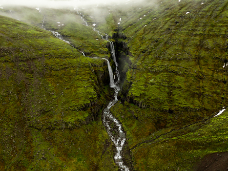 Aerial view of a waterfall cascading down a lush green mossy mountain slope in the Eastern Region of Iceland. Aerial view of a waterfall cascading down a lush green mossy mountain slope in the Eastern Region of Iceland.