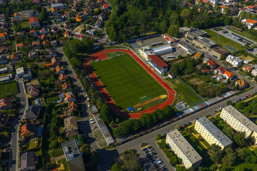 Aerial view of a sports stadium with a red running track and green grass field surrounded by residential houses apartment buildings and trees in Kyjov South Moravian Region Czechia.