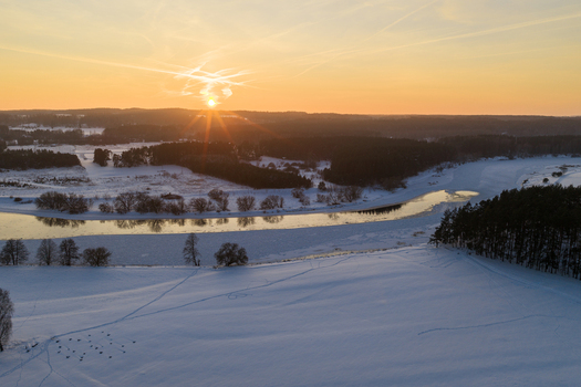 Aerial view of the snow covered landscape and frozen river winding through pine forests during a golden sunset Kernave Vilnius County Lithuania.